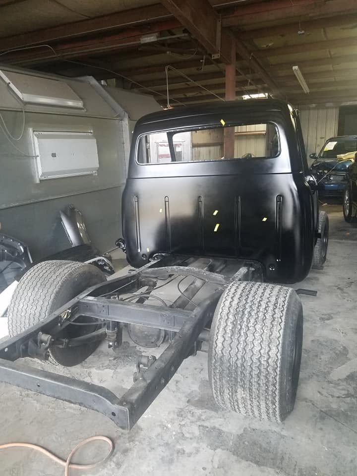 Classic pickup truck cab freshly painted black, sitting on the bare frame in the shop