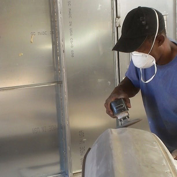 Technician in a dust mask sanding a repaired panel smooth