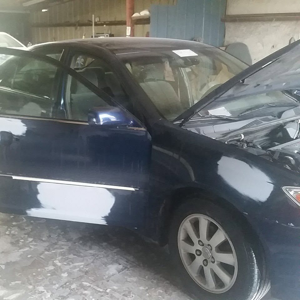 Dark blue Toyota Camry with gray primer over repaired spots on the door and front fender